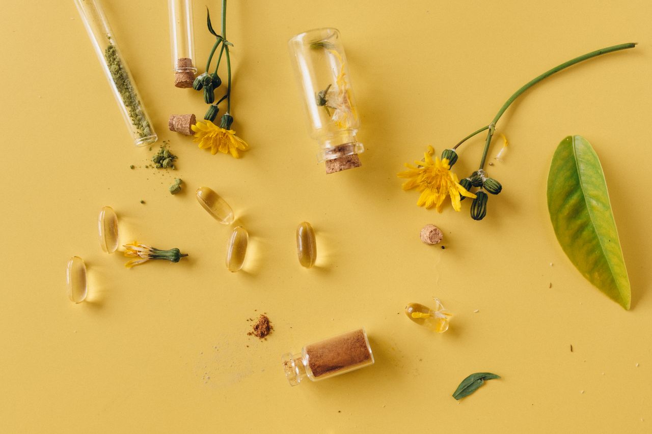 Services A flat lay of glass bottles, capsules, and flowers on a vibrant yellow surface, representing natural remedies.